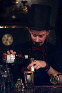 Barkeeper mit einer Flasche Tanqueray Gin und einem Barmaß.