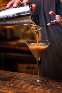 Espresso Martini Cocktail der durch ein Sieb in ein Martiniglas abgeseiht wird