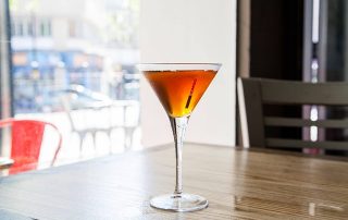 bernsteinfarbener Cocktail in einer Cocktailschale vor einem Fenster