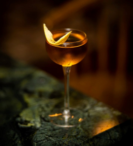 Bijou Cocktail mit Zitronenzeste auf Holzuntergrund