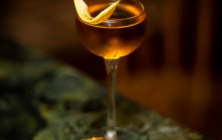 Bijou Cocktail mit Zitronenzeste auf Holzuntergrund