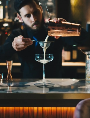 Barkeeper der einen Cocktail durch ein Sieb in eine Cocktailschale gießt