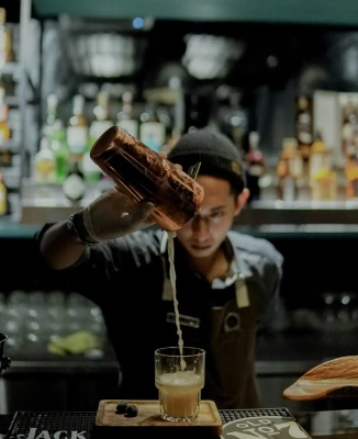 Barkeeper der einen Gin-Cocktail aus einem kupfernen Shaker Becher in ein Glas gießt.