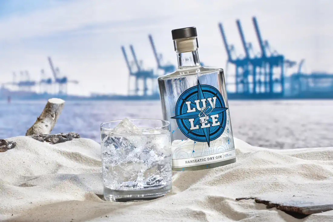 Luv & Lee Dry Gin mit Gin Tonic am Strand, im Hintergrund ein Hafen.