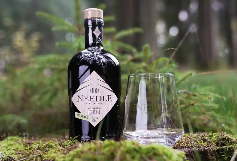 Needle Dry Gin mit Glas im Wald auf einem großen Stein