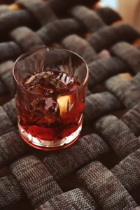 Roter Negroni Cocktail mit Zitronenzeste auf Rattanuntergrund.