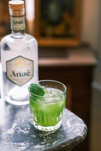 grüner Basil Smash Cocktail mit einer Flasche Anaë Gin im Hintergrund