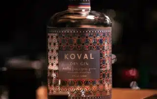 Flasche Koval Dry Gin auf Holztisch in dunklem Ambiente.