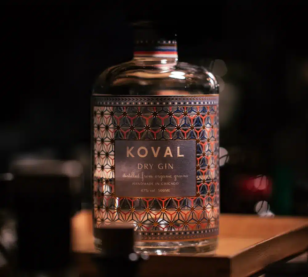 Flasche Koval Dry Gin auf Holztisch in dunklem Ambiente.