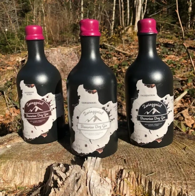 3 dunkle Zwinggeist Gin-Flaschen auf einem Baumstamm vor einer Waldkulisse
