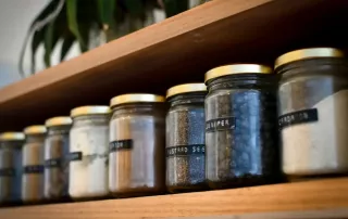 Verschiedene Gewürze in Gläsern in einem Holzregal.